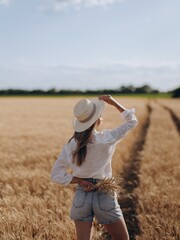 Young woman stands with bunch of wheat earls on field road leading across wheat field.
