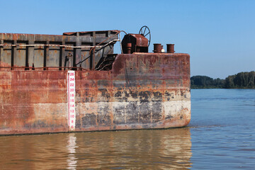 A close-up view of a corroded metal cargo barge stern on water