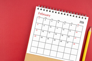 February 2026 desk calendar and pencil on red color background.