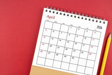 April 2026 desk calendar and pencil on red color background.