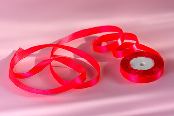 Spool of Raspberry Satin Ribbon for Gift Wrapping on Pink Background