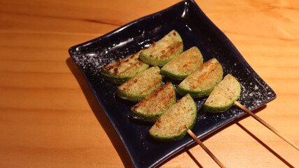 close up of two Japanese skewer grilled courgette pieces on a black plate n a izakaya restaurant with copy space
