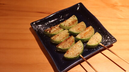 close up of two Japanese skewer grilled courgette pieces on a black plate n a izakaya restaurant with copy space