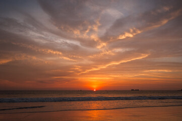The sun sets over the ocean, casting an orange glow on the water and clouds.