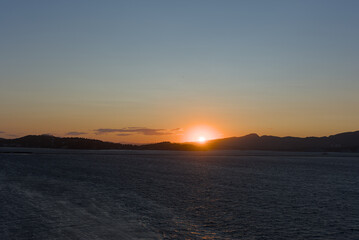 The setting sun creates a vibrant orange glow on the horizon, casting a soft light over the calm...