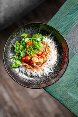 Black bowl with white rice topped with colorful vegetables, herbs, and sesame seeds. A fresh, appetizing Asian-style meal with vibrant ingredients and appealing presentation.
