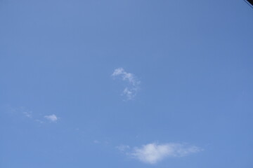 A serene view of a vast, clear blue sky on a sunny day with a few small, wispy white clouds floating peacefully.