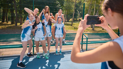 Young female basketball team taking a photo on an outdoor court. Concept of teen celebration, sporty lifestyle branding, active youth content, cheerful outdoor culture