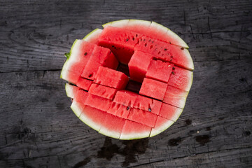 A top-down view of a refreshing watermelon, partially cut into juicy cubes, resting on a rustic...