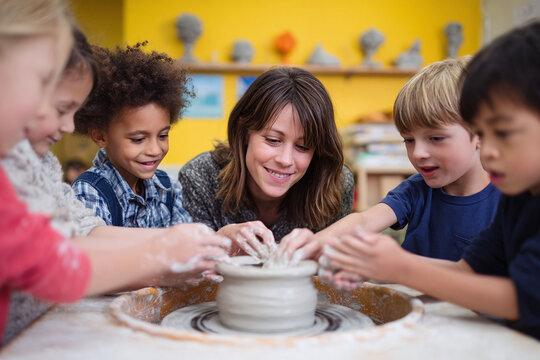 A diverse group of children learn pottery from their teacher. They are all touching clay on a wheel, smiling, and enjoying the process. Education, creativity, and teamwork concepts.