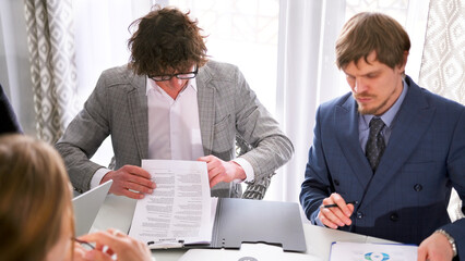 A handsome lawyer with glasses checks the documents before his client signs them. A man in a blue...