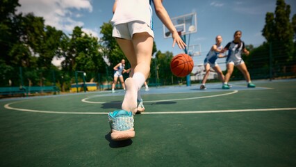 Women compete in basketball on outdoor court during a sunny summer day. Concept of motion and chase, fast-paced basketball moment, footwork training, dynamic movement focus, female athleticism