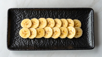 Freshly sliced banana pieces artfully arranged on a black textured rectangular plate