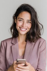 Naklejka premium A cheerful Latina woman with wavy hair wears a stylish blazer and smiles warmly while checking her smartphone. The bright indoor space reflects a positive atmosphere