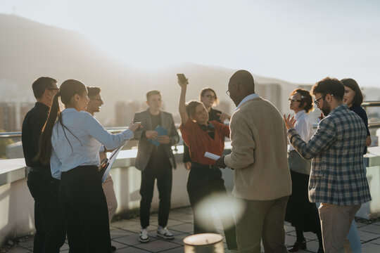A group of diverse business colleagues enjoy a celebration with music and dance on a rooftop, enjoying the sunset. The scene captures a joyful moment of teamwork and success.