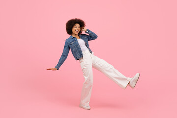 Smiling young woman talking on phone and walking in excitement. Studio image with pink background showing happiness and carefree lifestyle, copy space
