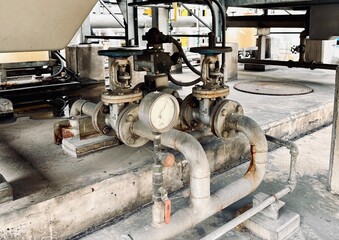 An old industrial piping system with pressure gauges and control valves on a concrete platform in a factory or wastewater treatment plant. Essential infrastructure for managing fluid processes.