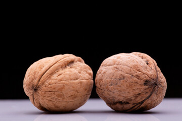 Two walnuts rest on a white surface