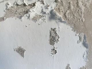 Damaged white painted wall surface with peeling paint exposing the concrete underneath