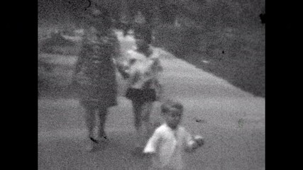 Archival film, Abstract family, mother, children walking by summer city street. Classic sixties quiet family lifestyle. Measured happy prosperous life together. Vintage old archive video. Retro 1960s