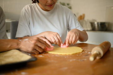 Close-up view of couple hands pressing pink cookie cutters into rolled dough on a wooden table in a home kitchen