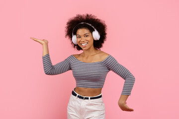 Cheerful young woman wearing wireless headphones, gesturing and dancing, smiling on pink studio background. Concept of modern audio lifestyle and fun expression, copy space