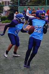 American football players in blue and black uniforms with the number 22 with the ball in their hands looking for someone to pass on on the green field at the stadium close-up	
