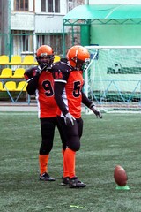 American football players in black and orange uniforms stand in the stadium during the game before kicking the ball	
