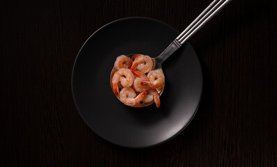 A dark image shows a spoon filled with cooked shrimp resting on a black plate