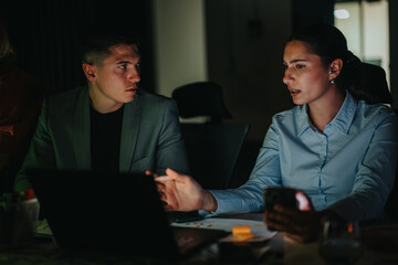 Two coworkers engaged in a serious discussion, focusing on project details during a late night...
