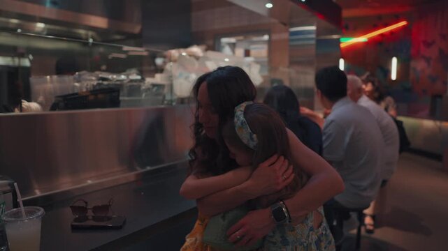 Mother and daughter warmly hugging inside a modern fast food restaurant