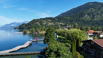 Naklejka premium Lakeside Promenade and Village with Wooden Piers and Mountain Backdrop in Summer