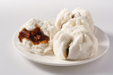 Three mini steamed pork bao on a white plate and white background