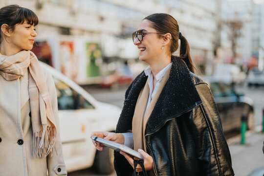 Two professional women sharing a lighthearted moment outdoors in an urban street setting.