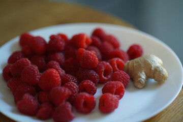 a white plate filled with red raspberries and a piece of ginger.