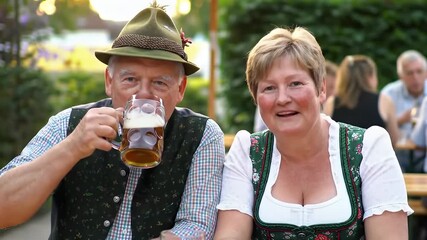 Happy senior couple celebrating Oktoberfest in traditional Bavarian attire.