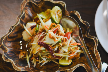 Somtam Thai or Somtam Fruit is a Thai salad made with shredded raw papaya or other fruits mixed with various seasonings, beautifully arranged in a uniquely carved wooden bowl.