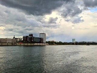 A European riverside city stands under a dramatic cloudy sky