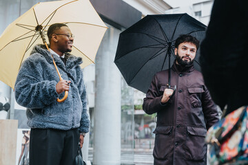 Two individuals having a conversation outdoors while holding umbrellas on a rainy day, conveying...