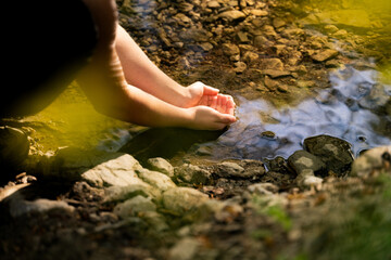 Close-up of a person hands touching clean river water from a mountain spring in forest in sunlight, outdoor hydration, eco lifestyle, nature conservation concept