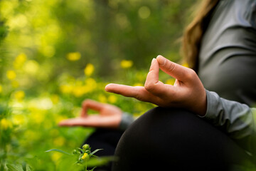 Woman practicing yoga with yellow flowers and green blurry background, doing Padmasana exercise, wearing sportswear, black pants and long sleeve, lotus pose with mudra gesture outdoors close-up