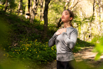 Portrait of young mindful woman practicing gratitude meditation in forest in sunlight, girl holding hands on her chest and enjoying nature with closed eyes, wearing black leggings and long sleeve