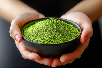 Woman's hands holding a black bowl filled with vibrant green matcha powder