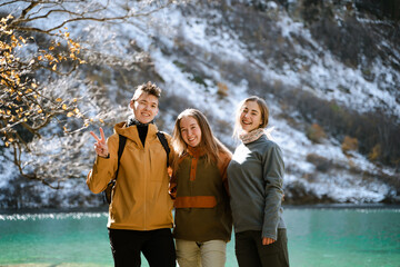 Three happy friends on a mountain lake on a sunny day, a group of tourists on a hike laughs, cheerful and carefree travelers smile