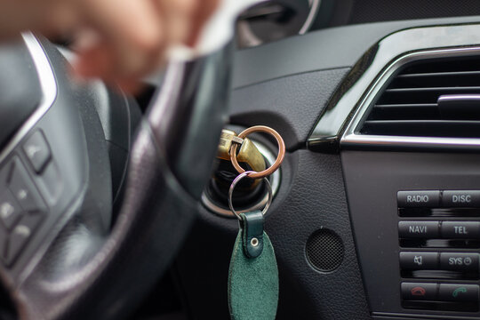 Close-up of a person's hand starting a car using a traditional metal key in the ignition, with dashboard controls visible. - Powered by Adobe