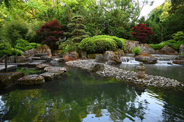 a beautiful Japanese garden with a pond surrounded by lush green trees, shrubs and flowers on a summer day