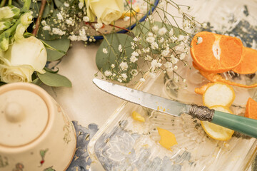Citrus slices and vintage knife on glass tray with white flowers and ceramic jar