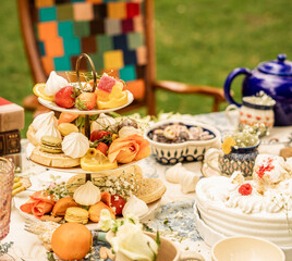 Tiered dessert stand with sweets fruit and meringue on floral tea table