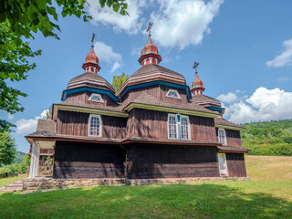 Wooden church in Nizny Komarnik, Slovakia. Side view with trees and wooden fence in a peaceful rural landscape. Traditional Carpathian religious architecture.
