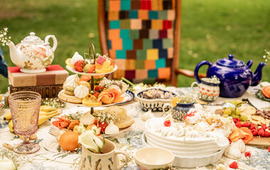 Colourful outdoor afternoon tea table with desserts fruits and teapots